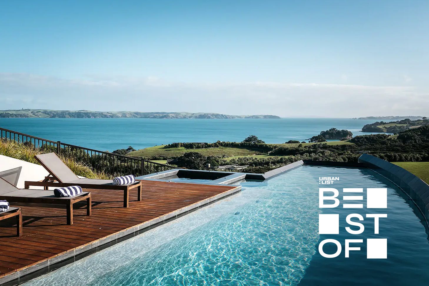 A stunning pool and row of deck chairs with stripy towels on them overlooking an incredible view of the Hauraki Gulf.